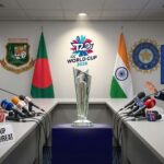 A tense press conference scene with two men seated at a long table, separated by a 2026 ICC T20 World Cup trophy. On the left, a man in a Bangladesh cricket jersey sits in front of a Bangladesh flag and a placard reading "WORLD CUP BOYCOTT THREAT". On the right, a man in a suit sits before an Indian flag and a screen displaying "IPL BROADCAST SUSPENDED". Microphones from various news agencies are present.